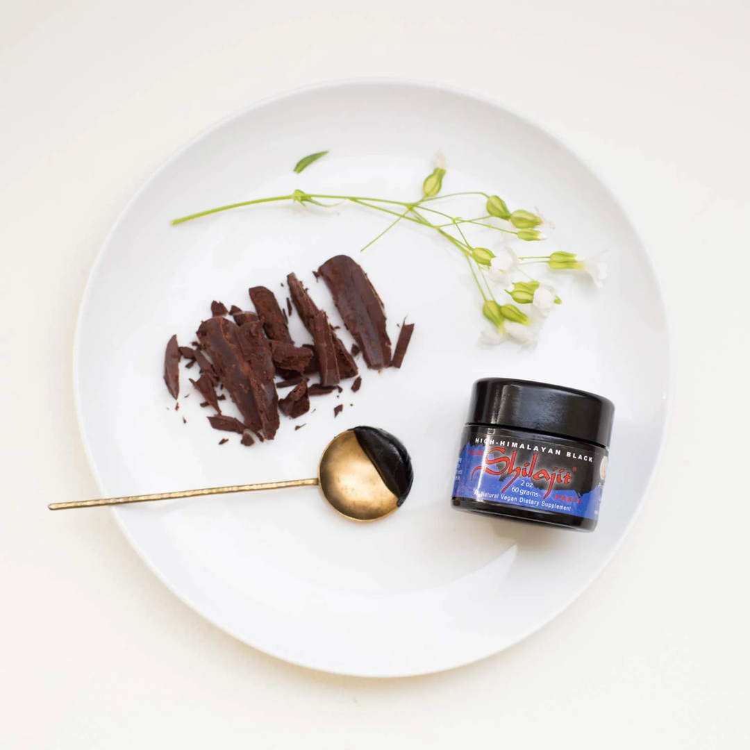Bowl of dark chocolate with a spoon and a container labeled 'Shilajit' on a white plate.